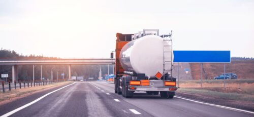 Camión cisterna transportando mercancías peligrosas se aleja en la carretera al atardecer