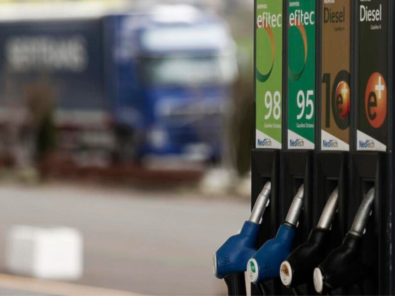 Foto de surtidor de gasolinera con un camión azul y pixelado al fondo